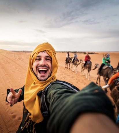 Happy tourist having fun enjoying group camel ride tour in the desert - Travel, life style, vacation activities and adventure concept